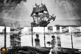 New York Wedding Portrayed in Black and White with Reflection in Majestic Tall Ship Painting Captured in a black and white portrait at a New York wedding, the couple's reflection is seen in a painting of a majestic tall ship on the open sea.